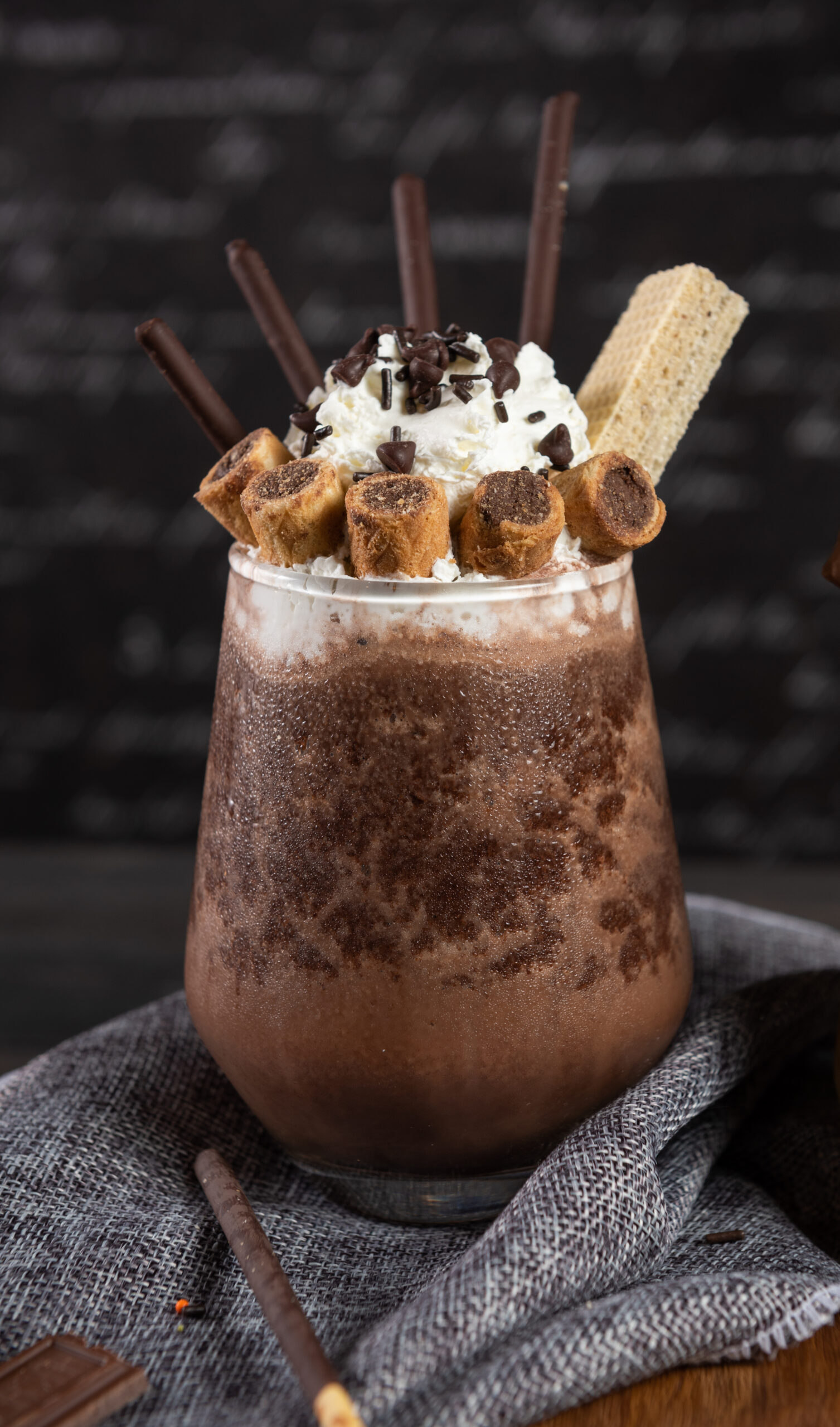 Chocolate smoothie, decorate toppings by many desserts such as bars, rolls, chocolate-coated and whipping cream in a clear glass on a dark gray real wood. Popular drink to quench thirst to cool down
